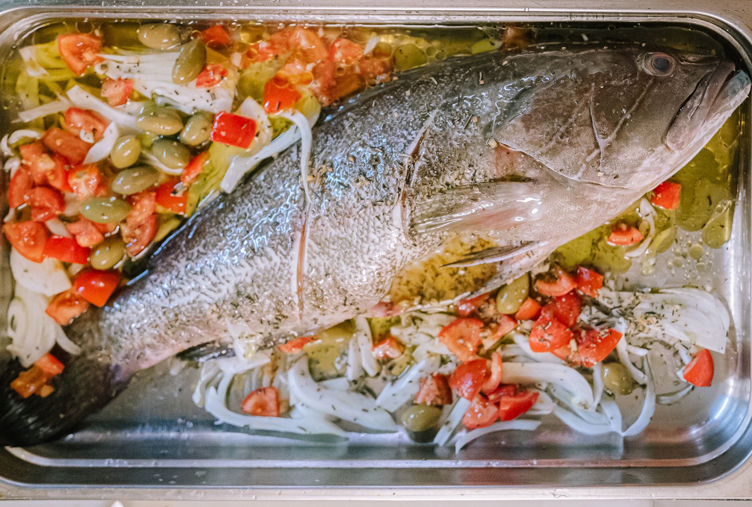 Pesce intero pronto per il forno con pomodorini e cipolla